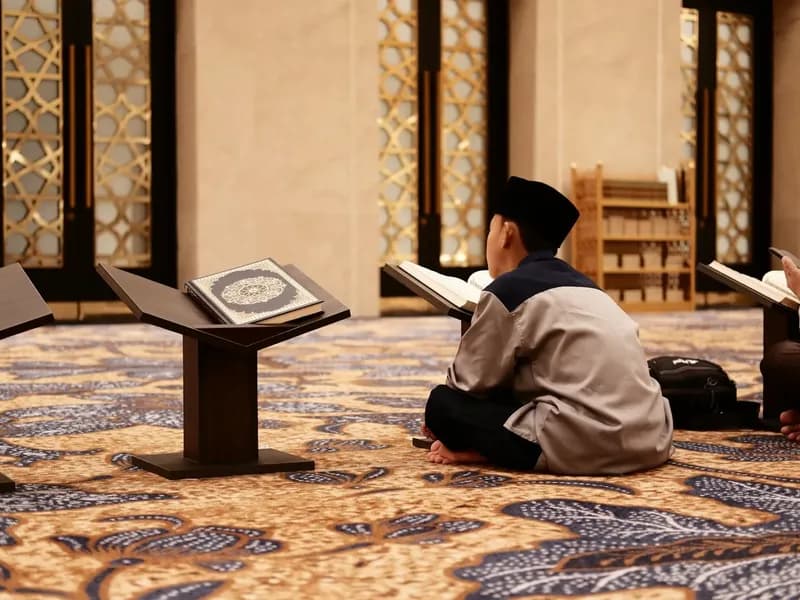 Young readers seated with Qurans on wooden stands inside a mosque.