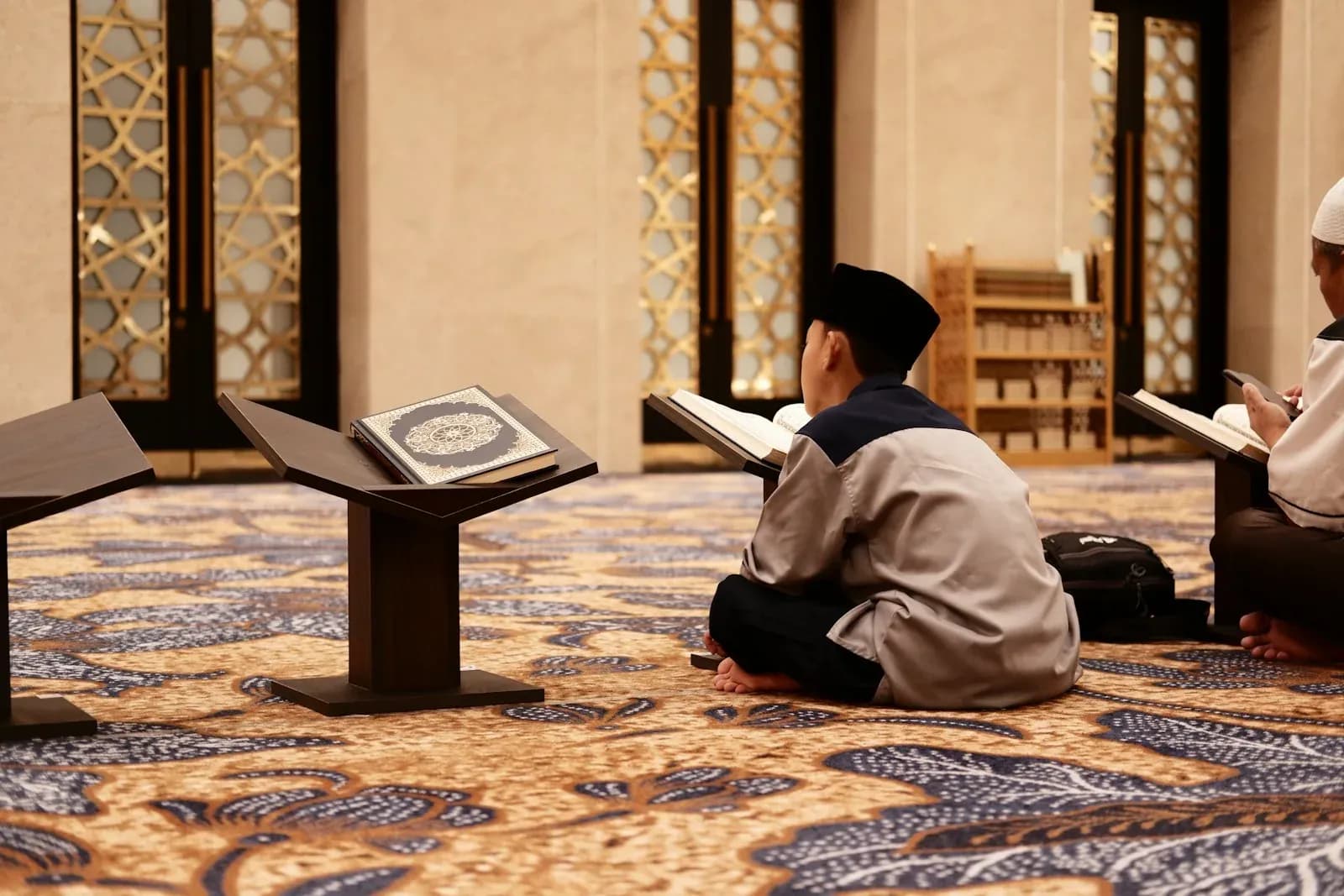 Young readers seated with Qurans on wooden stands inside a mosque.