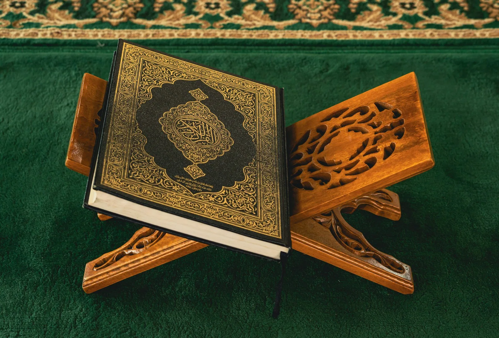A gold patterned Quran resting on a carved wooden stand on a green carpet