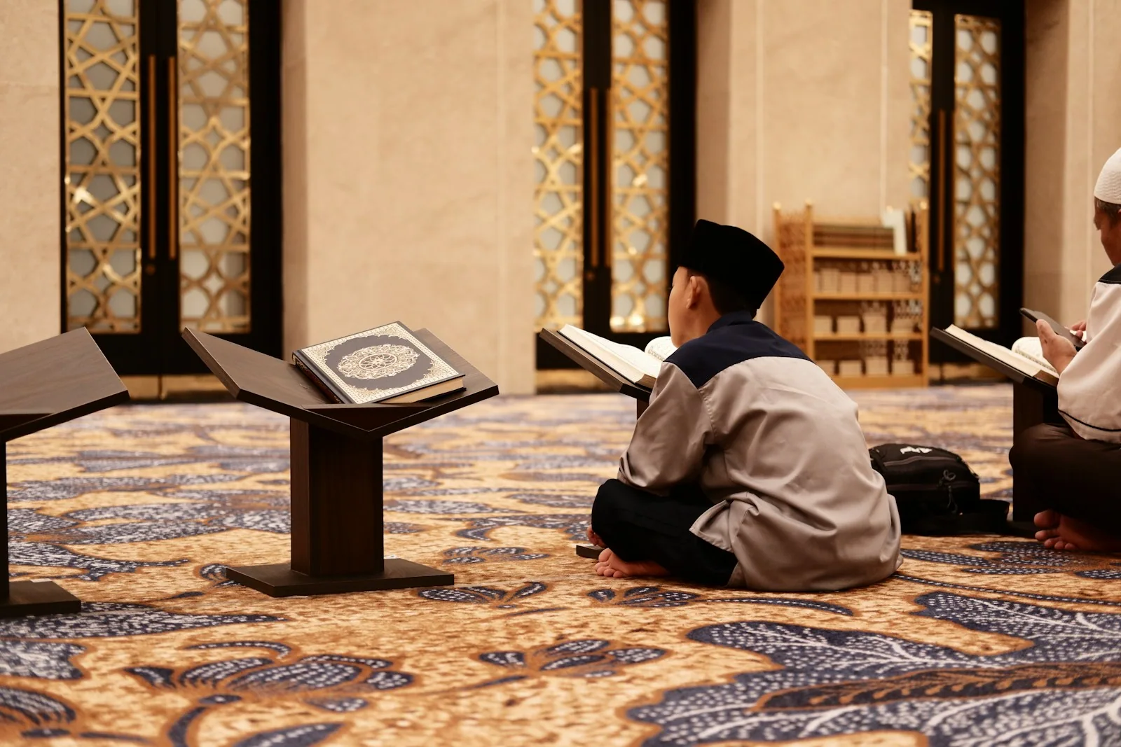 Young readers seated with Qurans on wooden stands inside a mosque